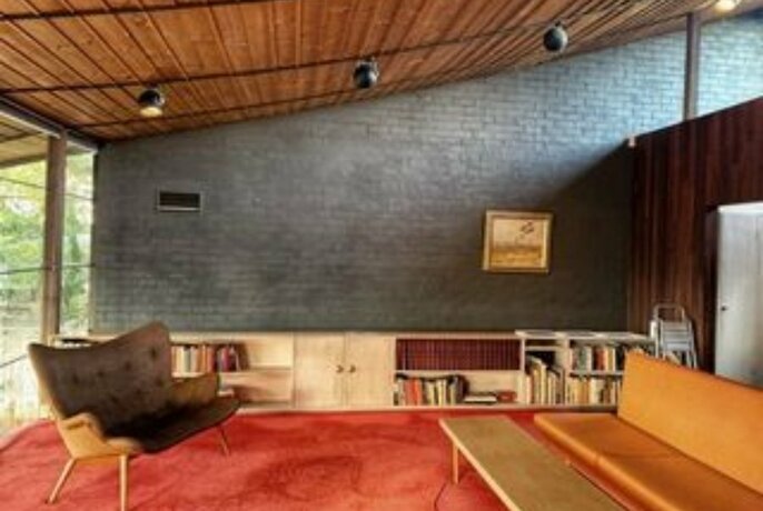 Lounge room of Robin Boyd's Walsh Street house, with wooden angled ceiling, brick interior wall, red carpet and built-in furnishings.
