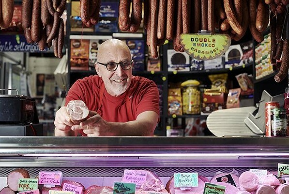 Proprietor in a shop with Polish sausages hanging and a range of cured meats on display.