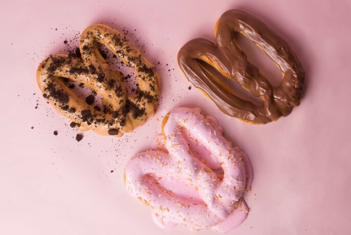 Three pretzels covered in chocolate, pink icing and sprinkles.