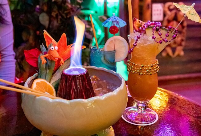 A collection of tropical drinks including a flaming volcano and cocktails with beads and umbrellas on them. 
