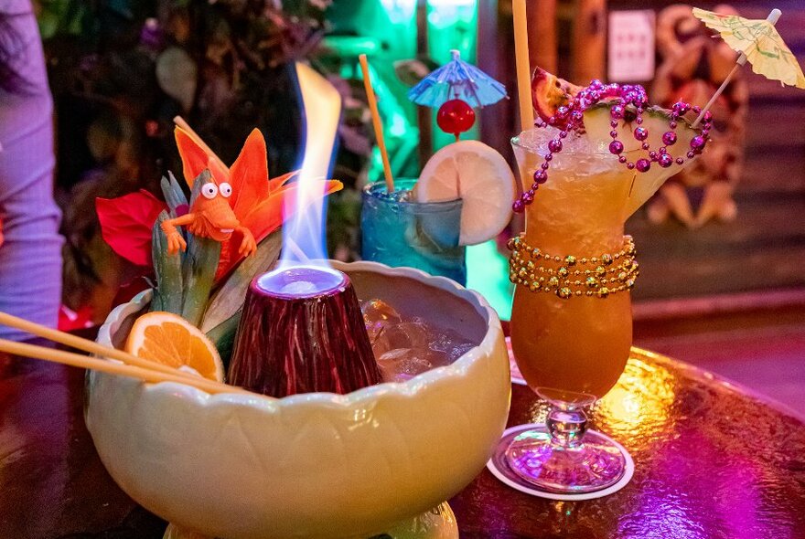 A collection of tropical drinks including a flaming volcano and cocktails with beads and umbrellas on them. 