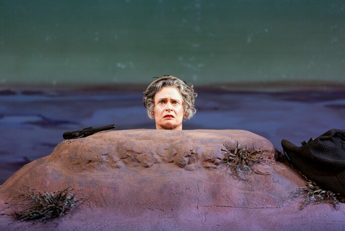 Performer Judith Lucy from the head up, the rest of her body buried in a small hill, on a stage.