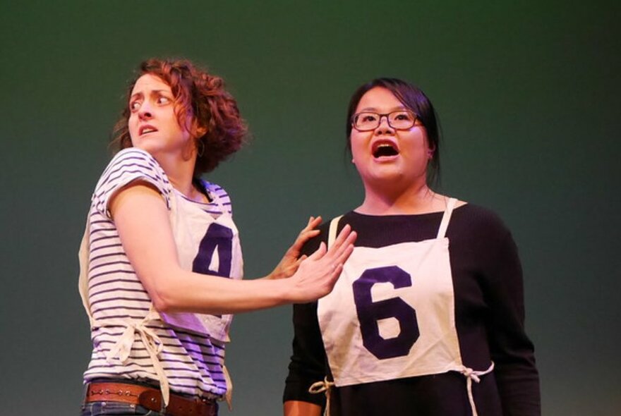 Two people on a stage interacting with one another, each wearing a numbered bib over their torso.