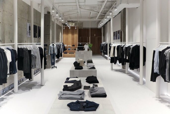 A minimalist clothing store with black, white and grey clothing on racks and tables. 