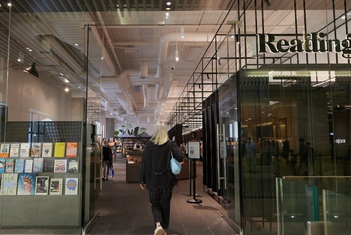Person walking through the glass entrance to the Readings Emporium store with shop signage partially visible on the window.