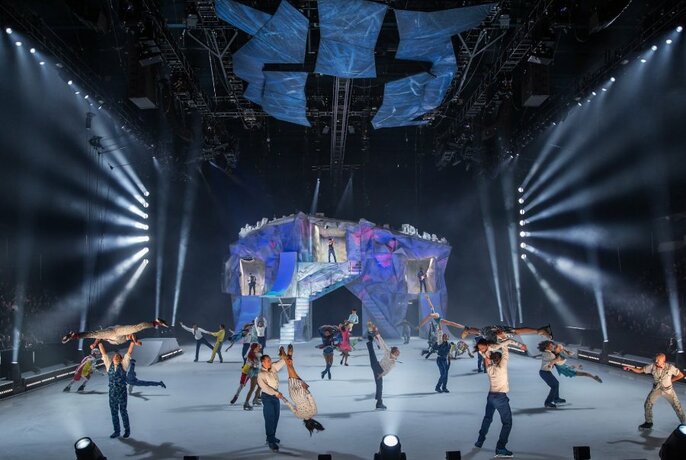 Multiple performers on an ice stage with a light display in the background. 