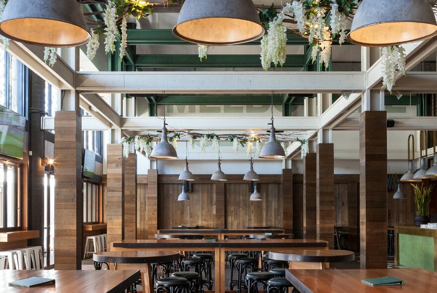 Empty interior of Melbourne Public showing tables, stools and overhanging lights and plants.