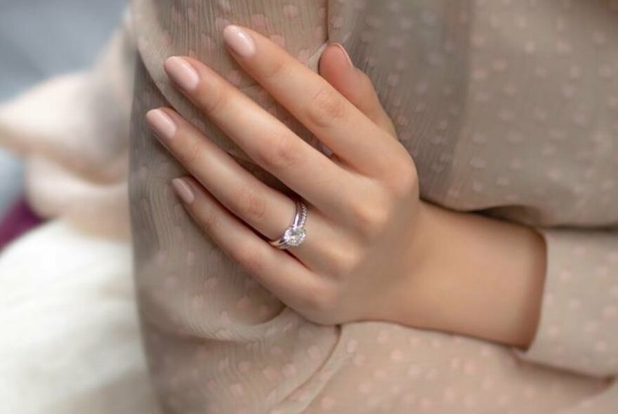 A woman's hand with a diamond ring, resting on her arm.
