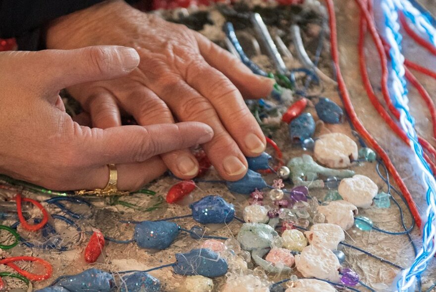 Close up of two hands touching some threaded gemstones and rocks. 