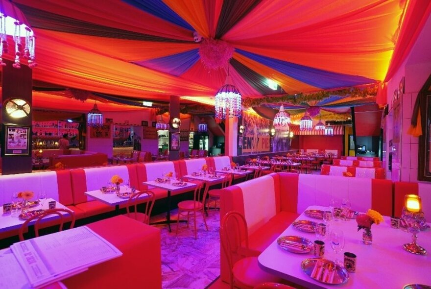 Interior of an Indian restaurant with red tones and a circus tent-like ceiling. 