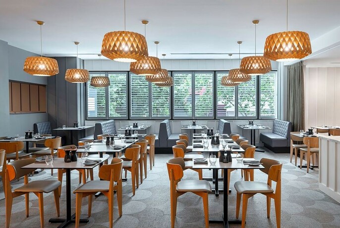 Bright dining room filled with rows of tables and chairs, lit by overhead wicker pendant lights.