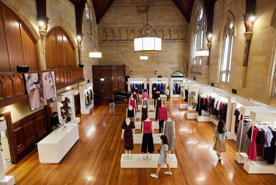 A woman walking through a retail shop in a cathedral with a dozen mannequins displaying clothing down the centre of the space.