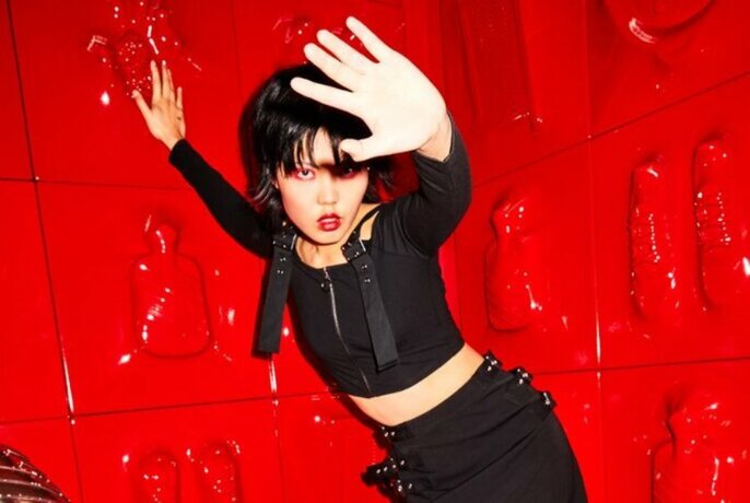A model posing wearing black strappy clothing in a red room. 