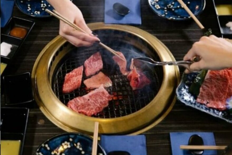 People cooking meat over a charcoal grill.