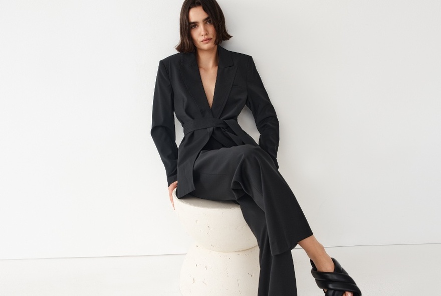 Model seated on a white stool wearing a dark suit.