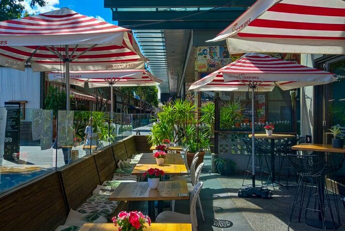 An outdoor dining area at the Common Man, with red striped umbrellas and wooden tables.