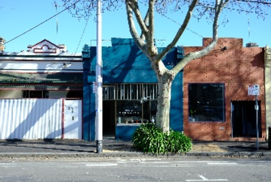 The pottery studio seen from the street, with a blue-painted brick exterior, large window and tree.
