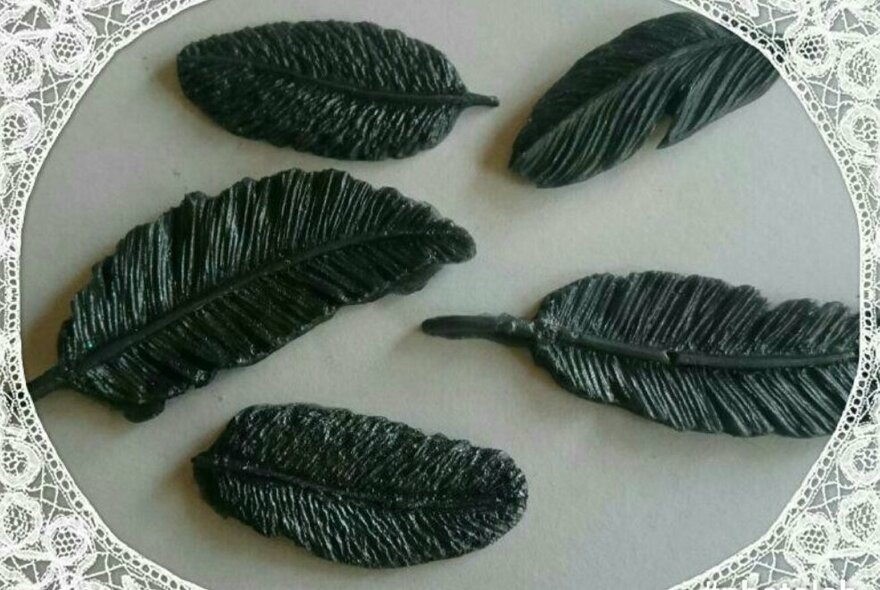 Four small black bars of soap in the shape of feathers.