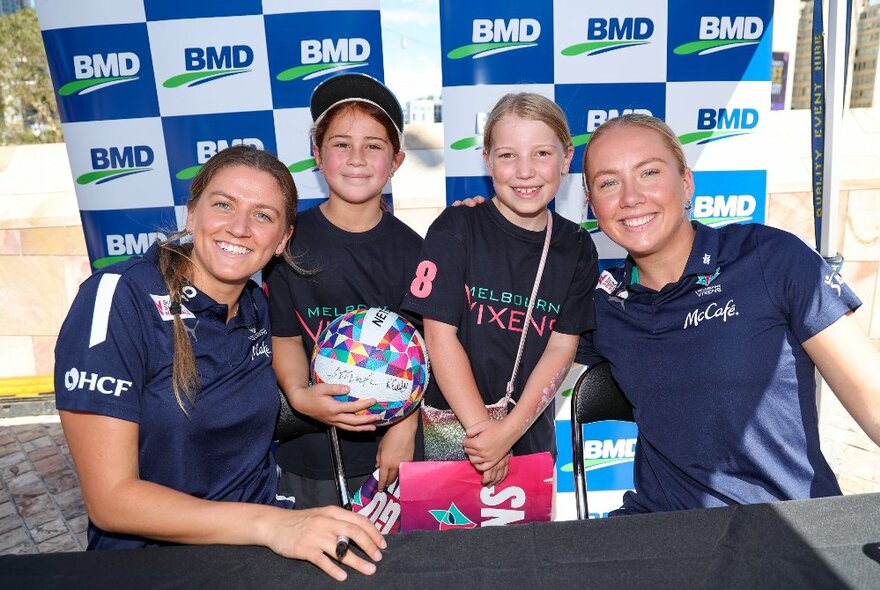 Two Melbourne Vixens netball players and two young fans posing for a photo.