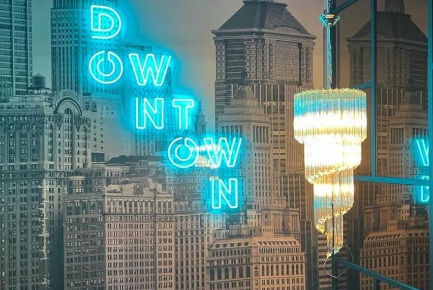 Chandelier and neon signage against wallpaper of city buildings.