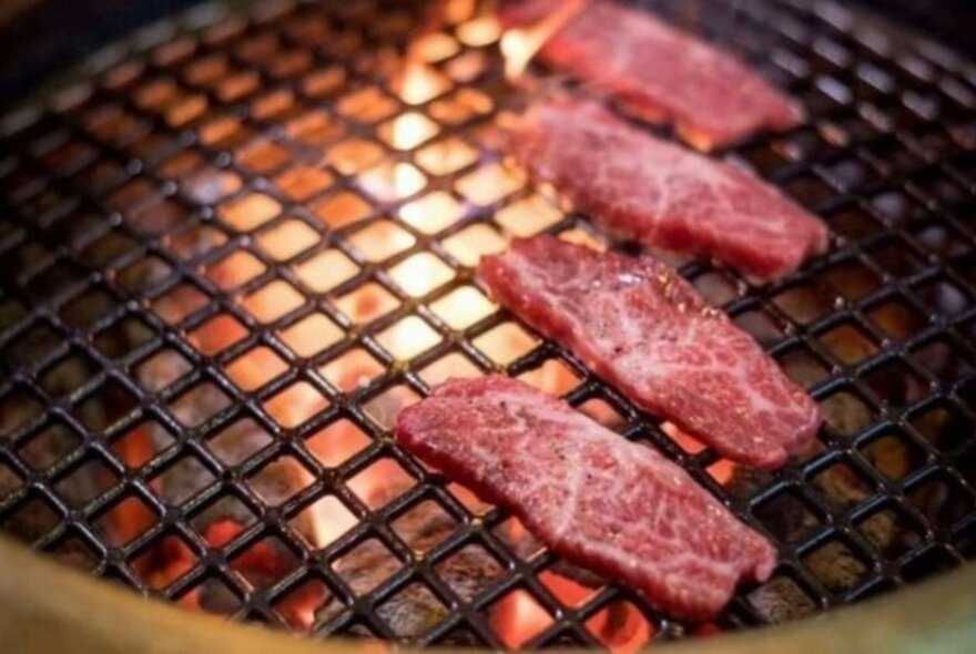 Slices of meat cooking over a charcoal grill.