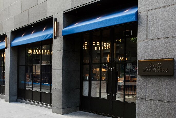 Exterior of restaurant Grill Americano, showing windows and blue awnings.