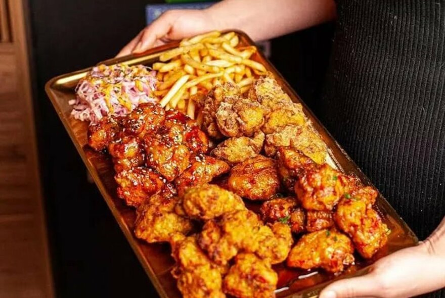 Hands carrying a plate of cooked crispy chicken pieces.
