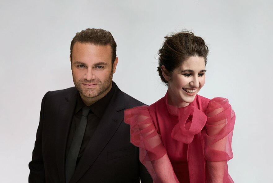 Opera stars, Nicole Car wearing a red blouse and Joseph Calleja wearing a black suit, in front of a light grey background.