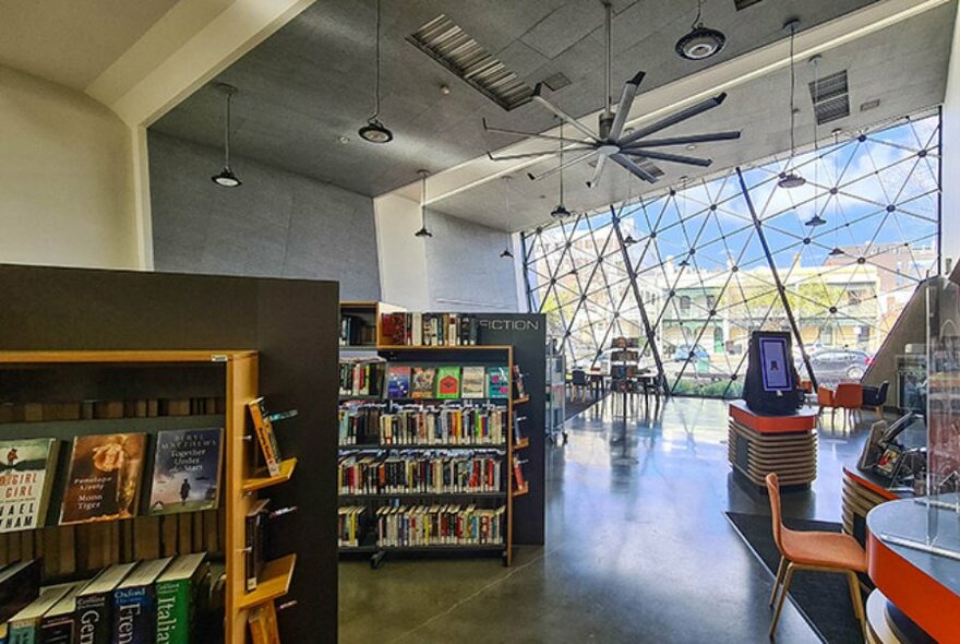 Interior of a library with bookshelves and a huge ceiling fan and a large feature window.