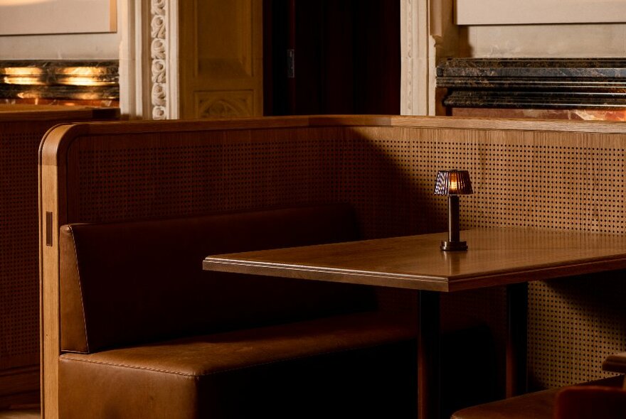 Corner dining booth, with dark leather bench seats and a small table lamp. 