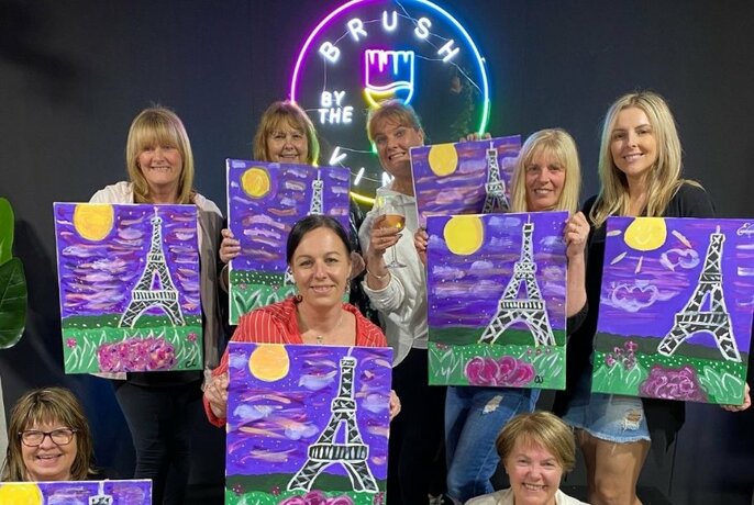 Group of people holding up paintings of the Eiffel Tower.