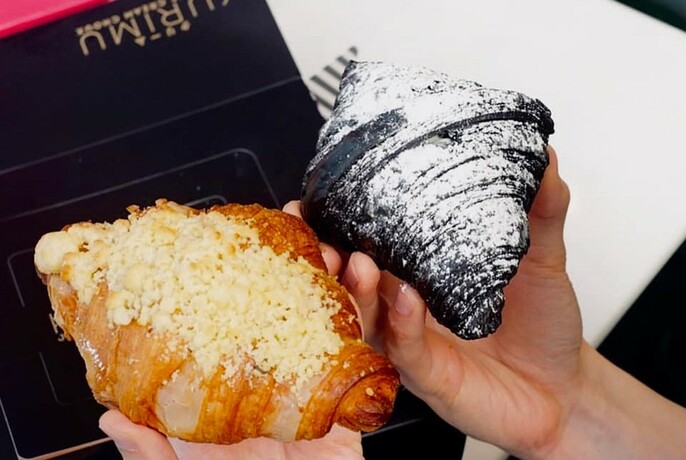 Two hands holding croissants, one plain, one dark chocolate. 