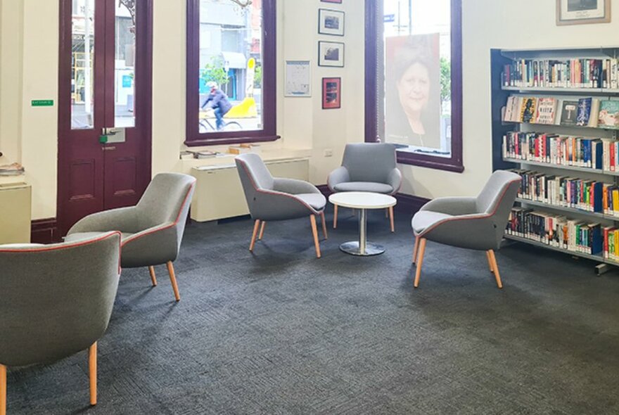 Individual grey armchairs, small tables and books in the interior of North Melbourne Library.