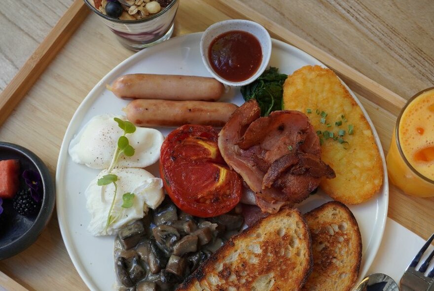 Overhead view of a big breakfast plate of poached eggs, bacon, sausages, mushrooms, tomato, a hash brown and toast.