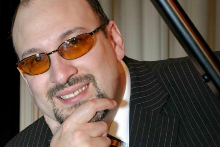 Head shot of pianist Marian Petrescu with hand hand on his chin, wearing sunglasses.