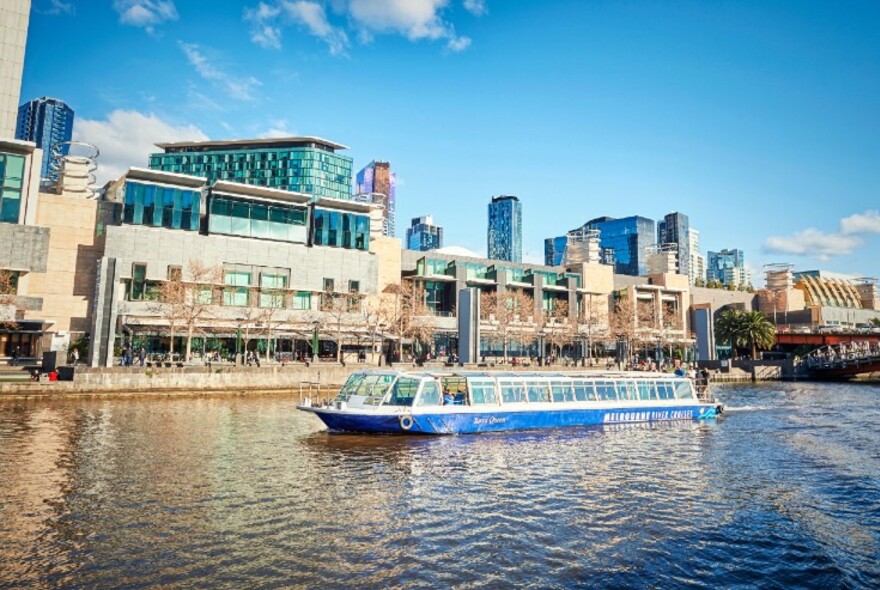 Enclosed ferry cruising the Yarra River with city skyline in the background.