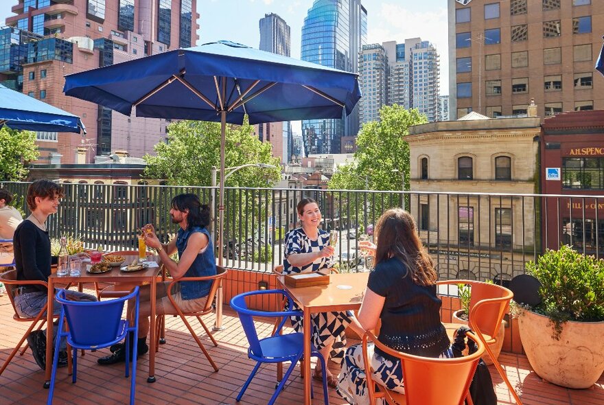 A group of people are sitting on a rooftop bar drinking cocktails and eating snacks