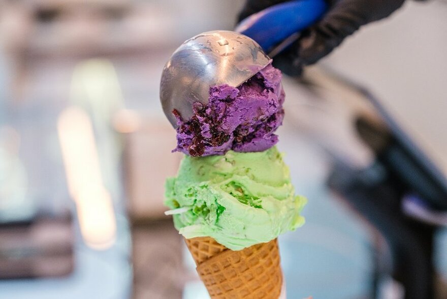 Someone scooping colourful ice cream into a waffle cone.