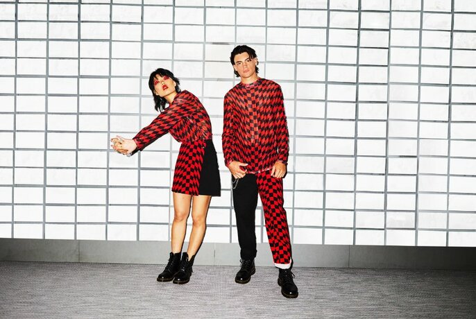 Two models in geometric red and black outfits, posing in front of a tiled wall