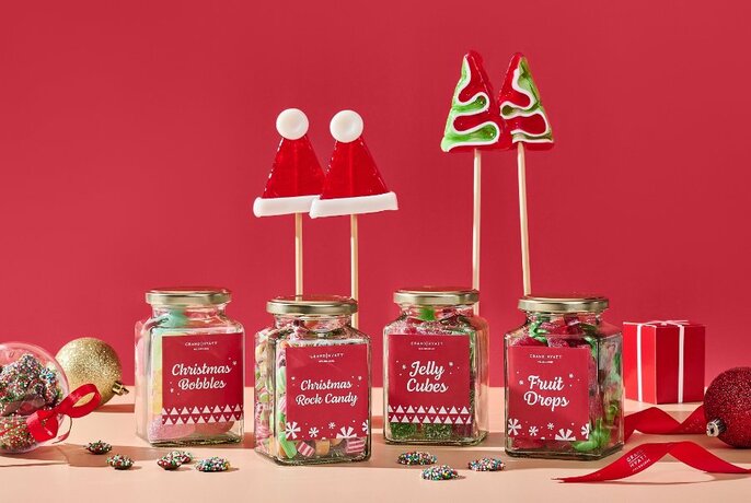 Jars of Christmas sweets and popsicles on a table against a red background.