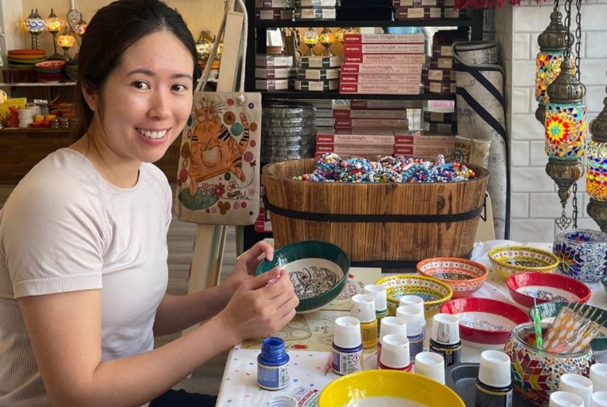 A person holding a bowl and paints at a workshop table with pots of paint.