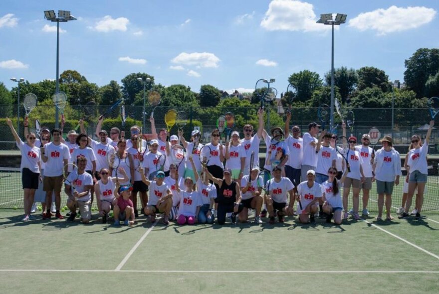 A large group of people posing for a group photo on a tennis court.