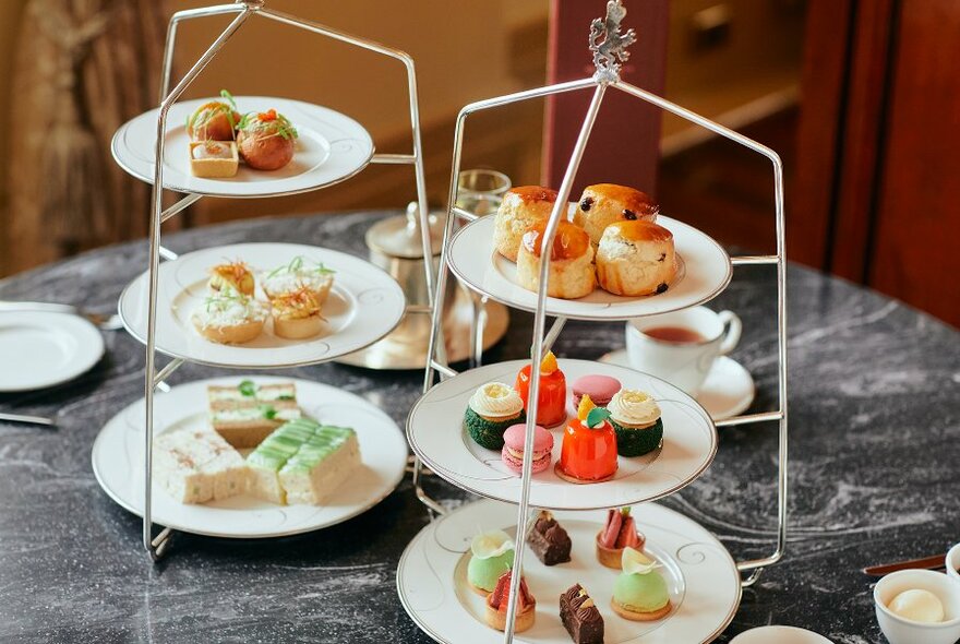 Afternoon tea with little plates of savoury and sweet food stacked up above each other on three-tiered stands.