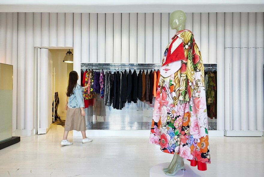 A woman is looking at clothes in a store there is a mannequin wearing a kimono in the store