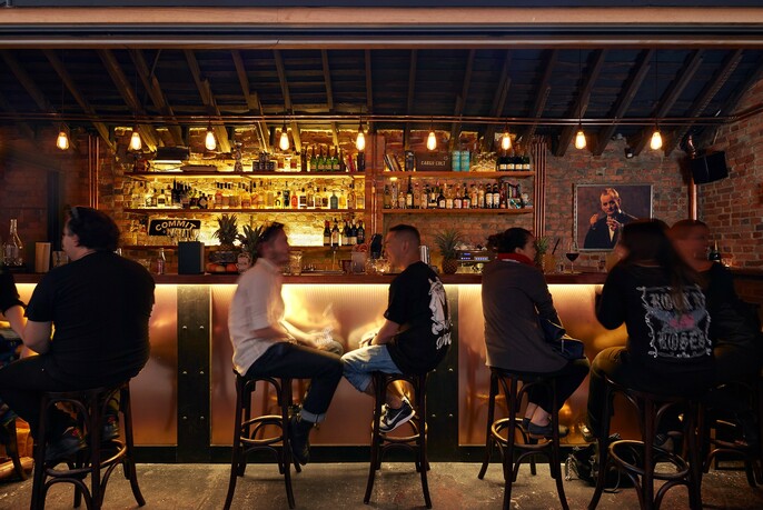 Dimly-lit interior of a group of people on stools in front of a well-stocked bar.