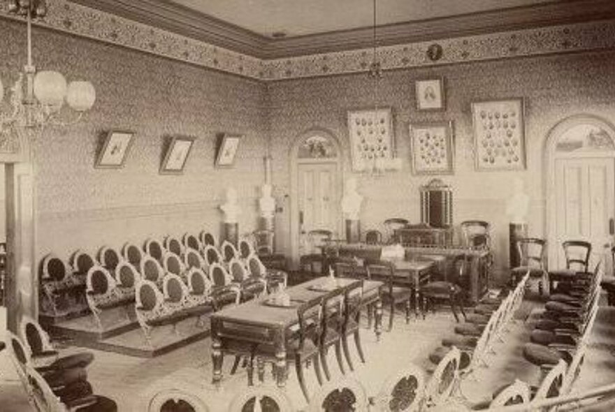 Sepia photo of a grand Trades Hall chamber with rows of seating around a central table and chairs.