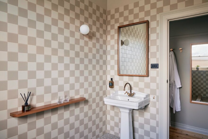 A bathroom decorated in a 1950s style with check tiles, a small white basin and large mirror.