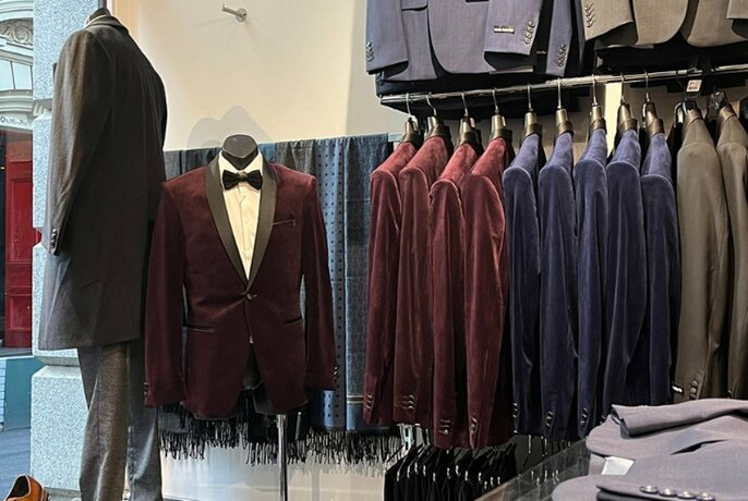 Interior of a menswear shop with a rack of burgundy and navy velvet suit jackets on display.
