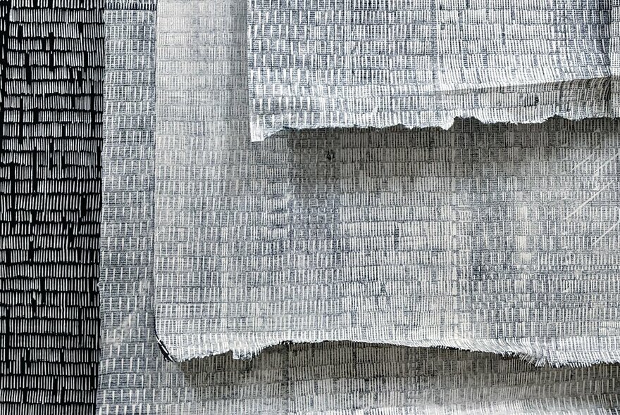 Sheets of light-weight washi paper in shades of grey and white, hanging vertically on top of each other.