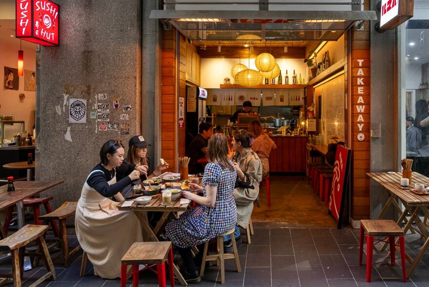 View from the street into a small and cosy interior of a cafe, a table of diners on the footpath and people also dining inside the small cafe.